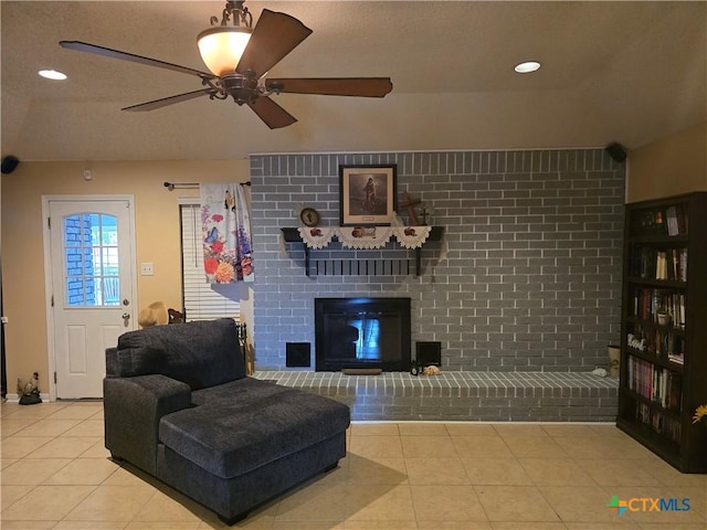 living area with tile patterned flooring, a ceiling fan, a brick fireplace, and a textured ceiling