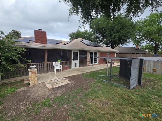 rear view of property featuring a yard, a chimney, roof mounted solar panels, and a sunroom