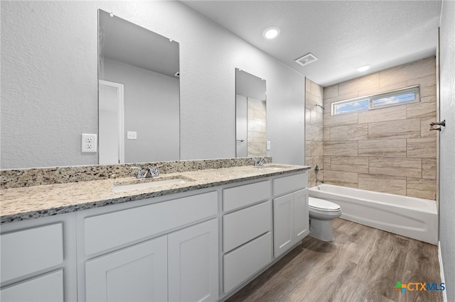 full bathroom with vanity, a textured ceiling, tiled shower / bath combo, hardwood / wood-style flooring, and toilet