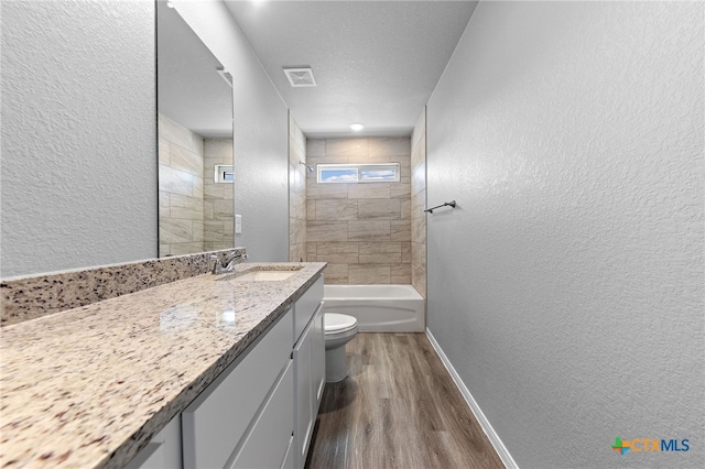 full bathroom featuring a textured ceiling, hardwood / wood-style floors, vanity, toilet, and tiled shower / bath combo