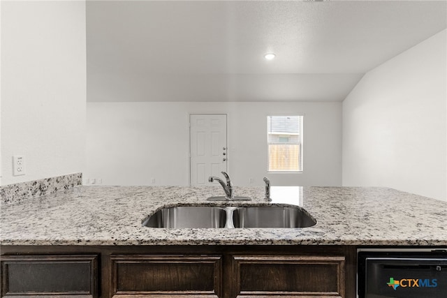 kitchen featuring light stone counters, dark brown cabinets, sink, and vaulted ceiling