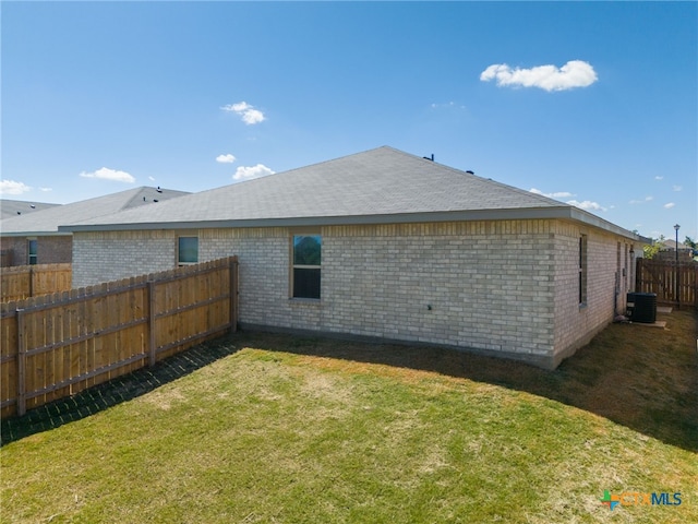 rear view of property with central air condition unit and a lawn