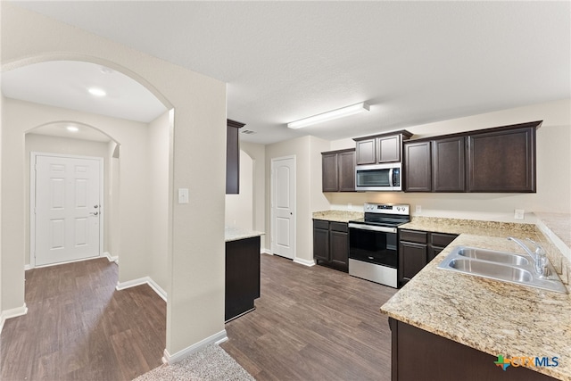 kitchen with light stone countertops, appliances with stainless steel finishes, dark brown cabinetry, sink, and hardwood / wood-style floors