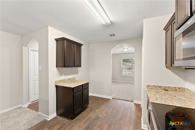 kitchen featuring dark brown cabinetry, visible vents, arched walkways, stainless steel microwave, and dark wood-style floors