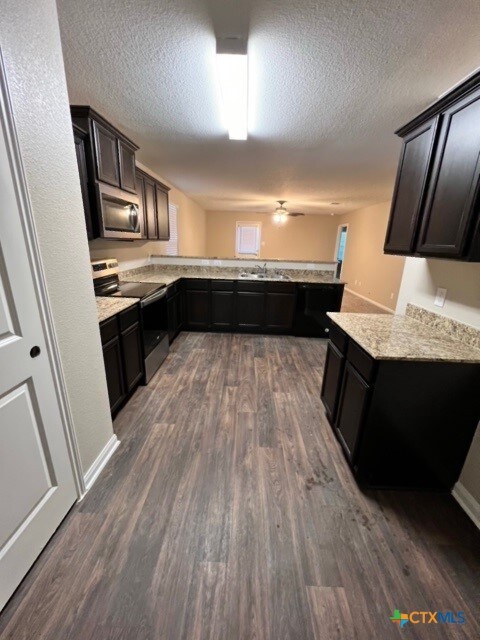 kitchen featuring light stone countertops, a textured ceiling, appliances with stainless steel finishes, dark hardwood / wood-style flooring, and kitchen peninsula