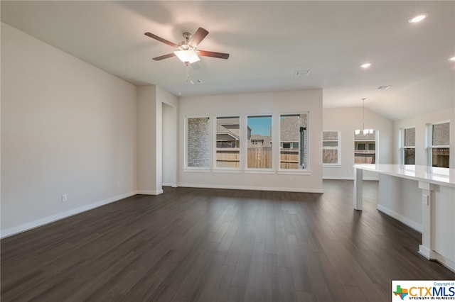 unfurnished living room with dark wood-type flooring, ceiling fan with notable chandelier, and vaulted ceiling