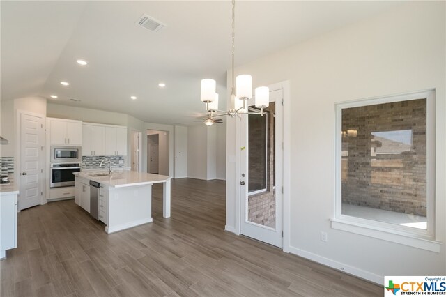 kitchen with white cabinets, sink, a kitchen island with sink, appliances with stainless steel finishes, and decorative light fixtures