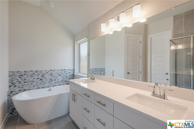 bathroom with tile walls, tile patterned floors, vanity, independent shower and bath, and vaulted ceiling