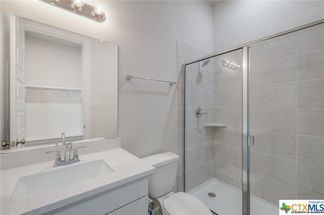 bathroom featuring toilet, vanity, and a shower with door