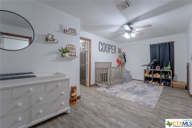 bedroom with ceiling fan, light hardwood / wood-style floors, and a crib