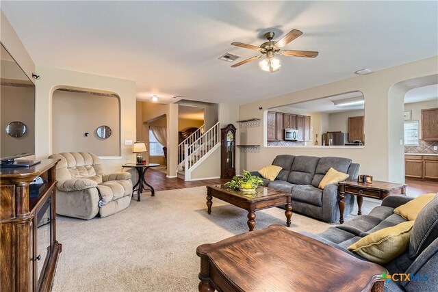 living room featuring ceiling fan, carpet floors, arched walkways, stairs, and visible vents