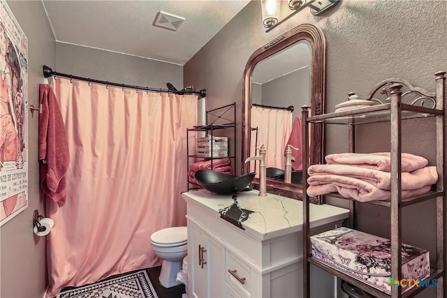 bathroom featuring visible vents, curtained shower, vanity, toilet, and a textured wall