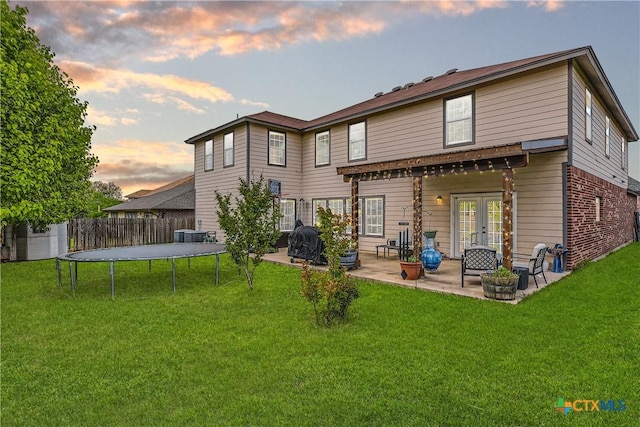 back of house featuring french doors, a trampoline, a lawn, fence, and a patio
