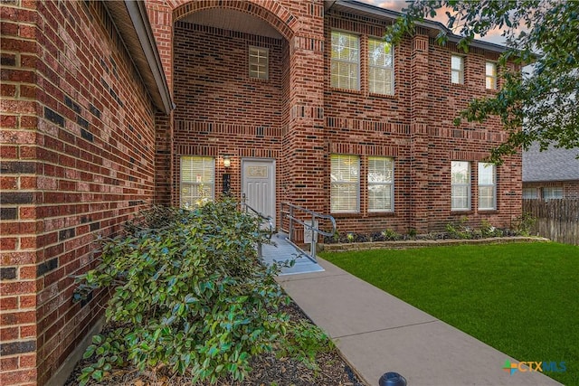 view of exterior entry with a lawn, brick siding, and fence