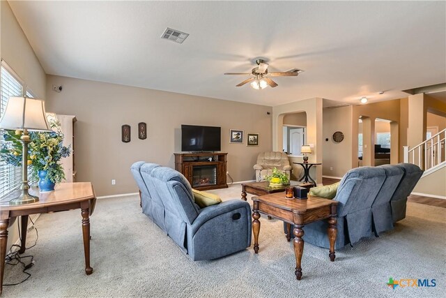 living room featuring ceiling fan, light colored carpet, arched walkways, baseboards, and visible vents