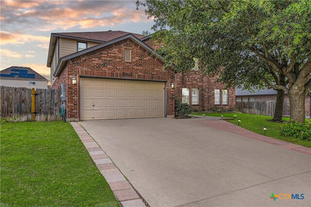 traditional-style home featuring driveway, a lawn, brick siding, fence, and an attached garage