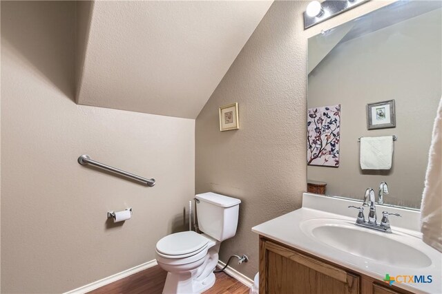 bathroom with wood finished floors, vanity, baseboards, toilet, and lofted ceiling