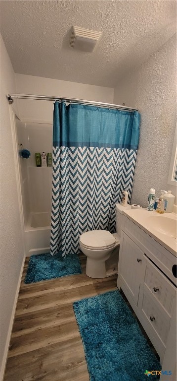 full bathroom with a textured ceiling, hardwood / wood-style floors, shower / bath combo with shower curtain, vanity, and toilet