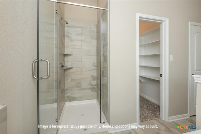 bathroom with a spacious closet, baseboards, a shower stall, and wood finished floors