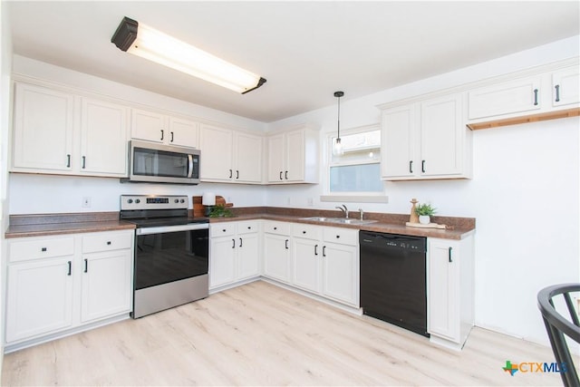 kitchen with dark countertops, appliances with stainless steel finishes, hanging light fixtures, white cabinetry, and a sink