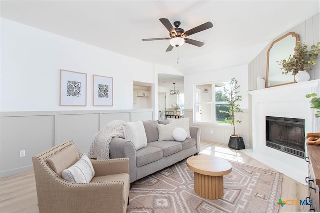 living area with a wainscoted wall, light wood finished floors, a decorative wall, a fireplace with flush hearth, and ceiling fan