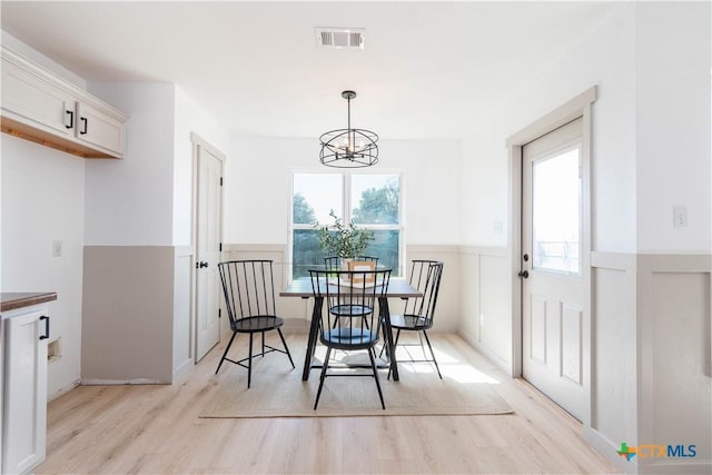 dining area featuring light wood-type flooring, a wainscoted wall, plenty of natural light, and a chandelier