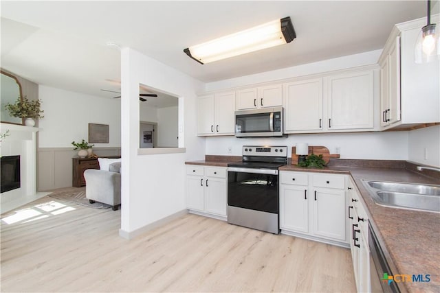 kitchen featuring white cabinets, dark countertops, open floor plan, stainless steel appliances, and a sink