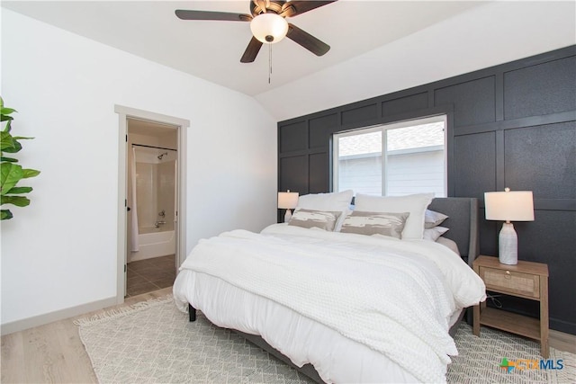 bedroom with ceiling fan, a decorative wall, wood finished floors, baseboards, and ensuite bath