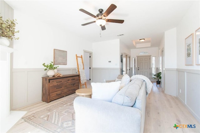 living room featuring light wood-type flooring, a wainscoted wall, and a ceiling fan