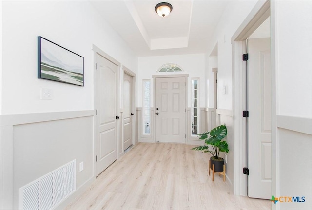 entrance foyer featuring light wood finished floors, visible vents, and a raised ceiling