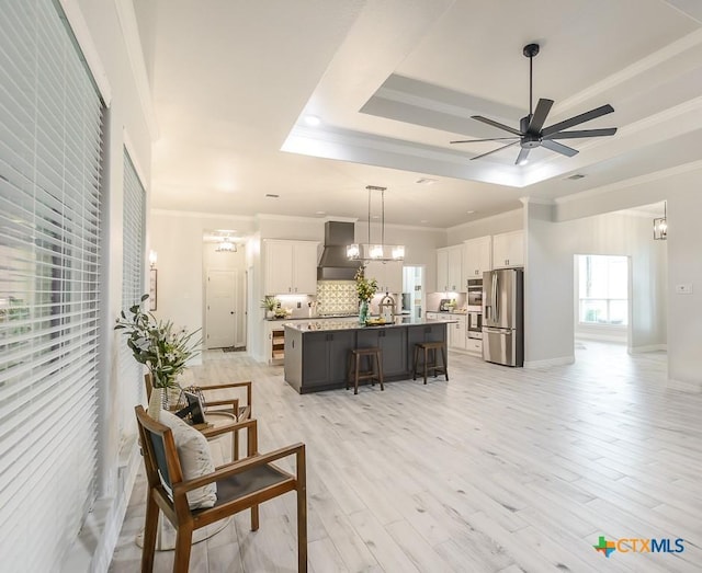 living area with a raised ceiling, a ceiling fan, ornamental molding, and light wood-style floors