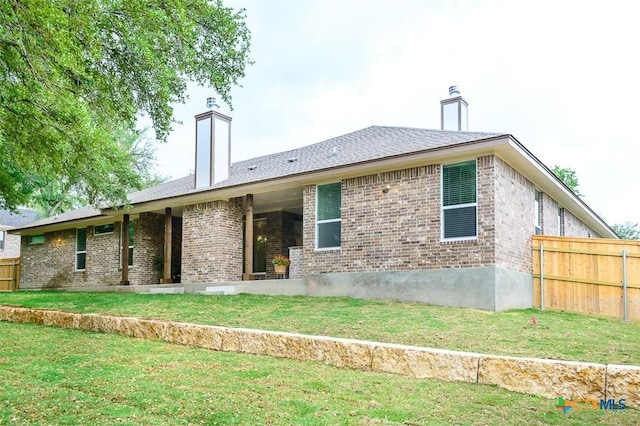 back of house with brick siding, fence, a lawn, and a chimney
