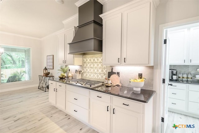 kitchen with stainless steel gas stovetop, decorative backsplash, custom range hood, white cabinets, and light wood finished floors