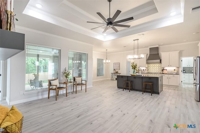 living room featuring a healthy amount of sunlight, visible vents, a raised ceiling, and ceiling fan with notable chandelier