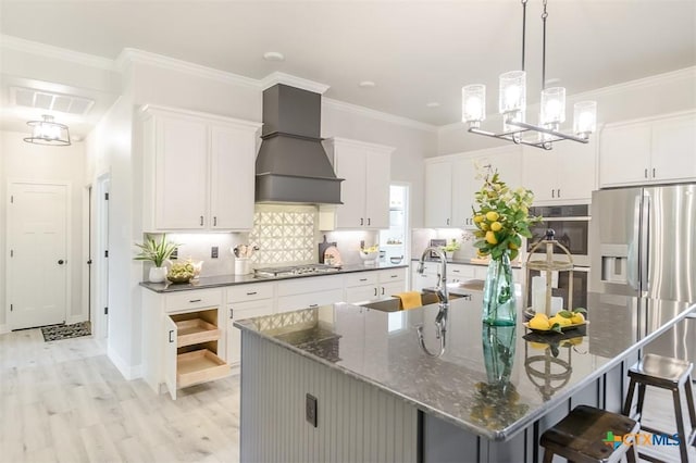 kitchen with a sink, stainless steel appliances, light wood-style floors, a center island with sink, and premium range hood