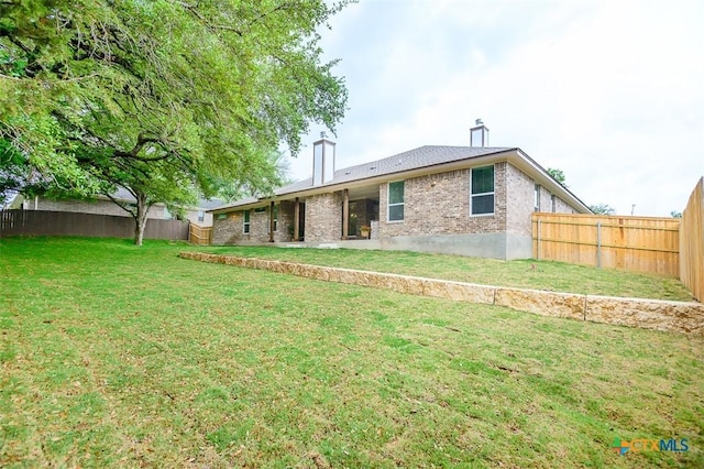 rear view of house with a chimney, brick siding, a fenced backyard, and a lawn