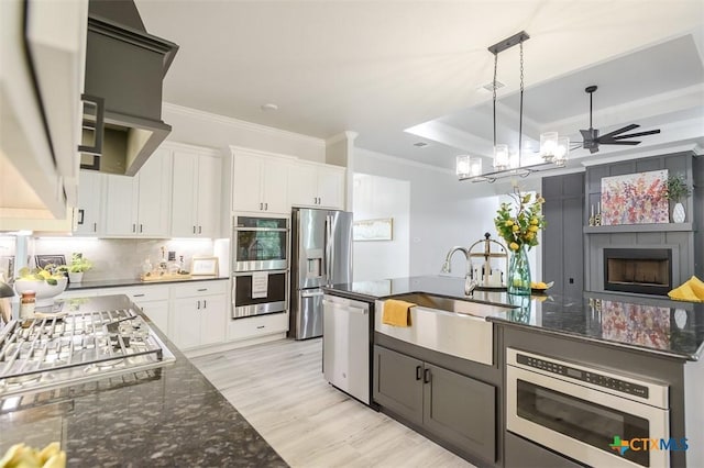 kitchen with appliances with stainless steel finishes, white cabinets, ornamental molding, a sink, and light wood-type flooring