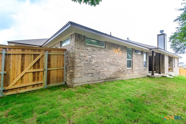 back of house with brick siding, a yard, a gate, a chimney, and fence