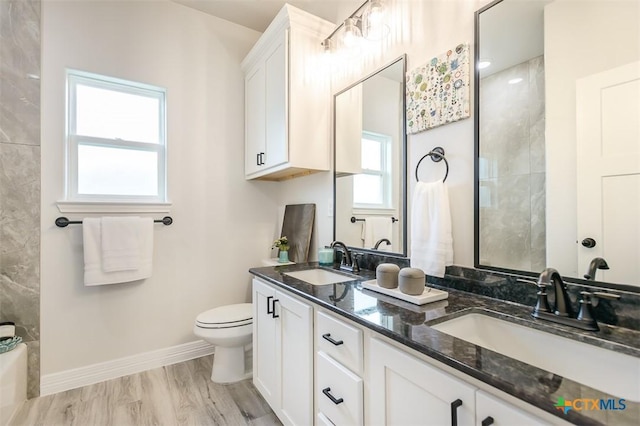full bath with baseboards, toilet, double vanity, and a sink