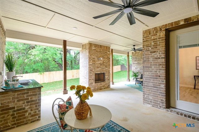 view of patio with an outdoor brick fireplace, a ceiling fan, and a fenced backyard