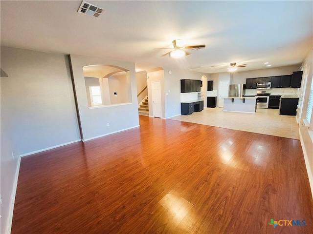 9200 Ashlyn Dr, Killeen, TX 76542 - unfurnished living room featuring ceiling fan, arched walkways, light wood finished floors, stairway, and healthy amount of natural light