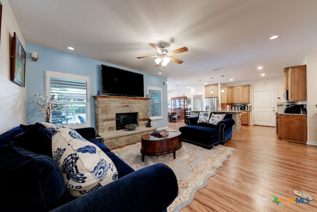 living room featuring a fireplace, light hardwood / wood-style flooring, and ceiling fan