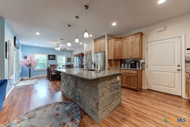 kitchen with an island with sink, light hardwood / wood-style floors, stainless steel fridge, and ceiling fan