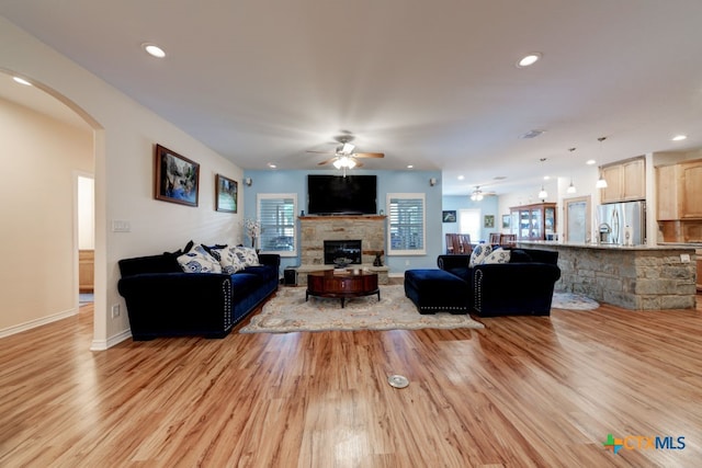 living room with light wood-type flooring, ceiling fan, and a fireplace