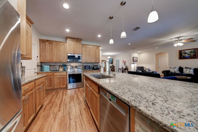 kitchen with appliances with stainless steel finishes, light hardwood / wood-style floors, decorative light fixtures, and light stone countertops