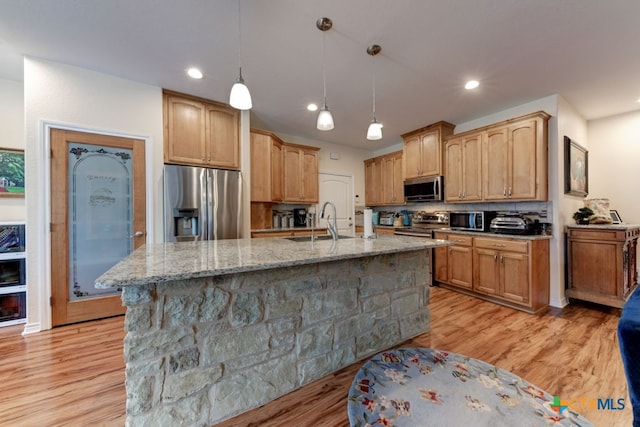 kitchen with light hardwood / wood-style floors, stainless steel appliances, a center island with sink, and backsplash