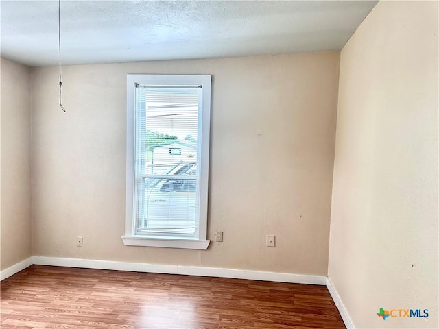 unfurnished room with a textured ceiling, baseboards, and wood finished floors