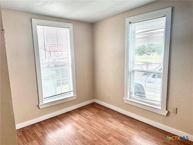 unfurnished room featuring plenty of natural light, wood finished floors, and baseboards