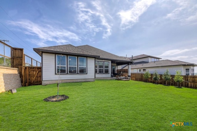rear view of house with a fenced backyard, roof with shingles, a yard, and a patio
