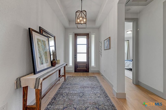 foyer entrance with a tray ceiling, baseboards, and light wood-style floors